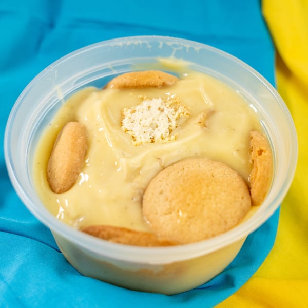 Banana pudding in a clear plastic container with vanilla wafers and crumbled topping.
