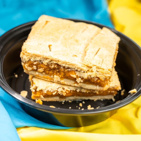 Two pieces of pumpkin pie in a black bowl, set against a blue and yellow fabric background.