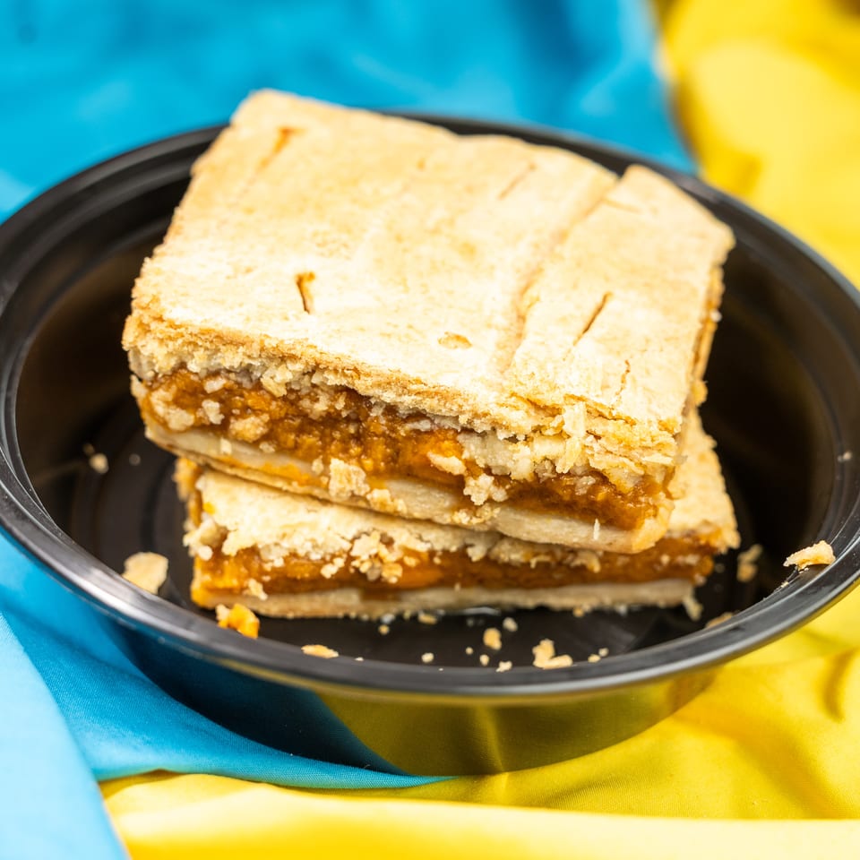 Two pieces of pumpkin pie in a black bowl, set against a blue and yellow fabric background.