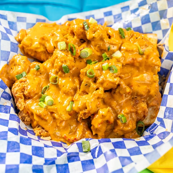 Crispy fried chicken pieces coated in a rich orange sauce and garnished with green onions in a checkered basket.