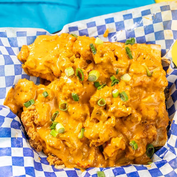 Crispy fried chicken covered in a creamy orange sauce and green onions, served in a checkered basket.