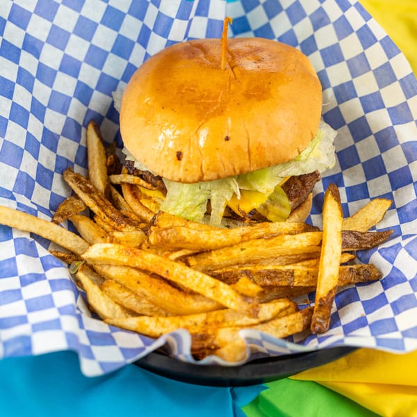 Cheeseburger with lettuce and pickles, served with seasoned fries in a blue and white checkered basket.