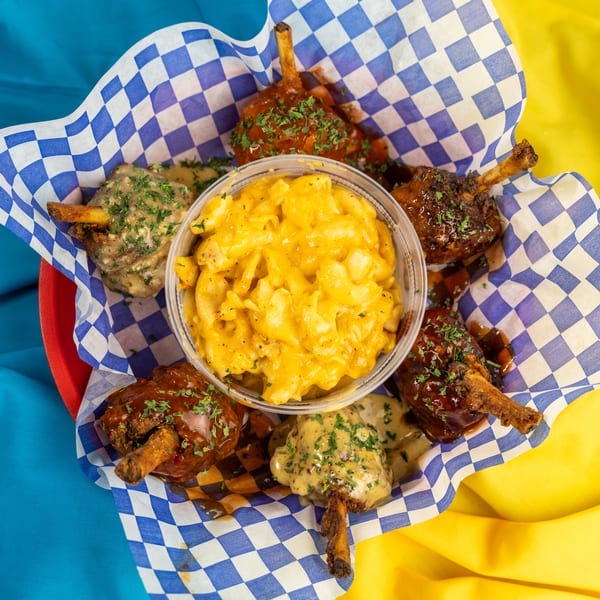 A basket of chicken lollipops with various sauces and a side of mac and cheese.