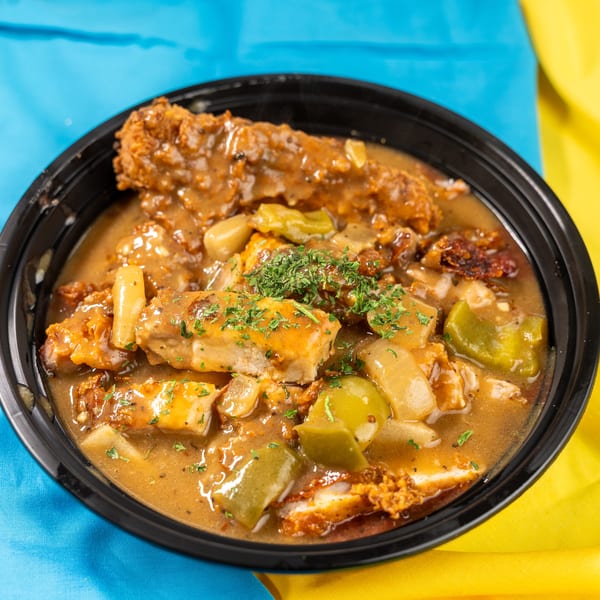 Hearty chicken and gravy with peppers and onions, garnished with parsley in a black bowl.